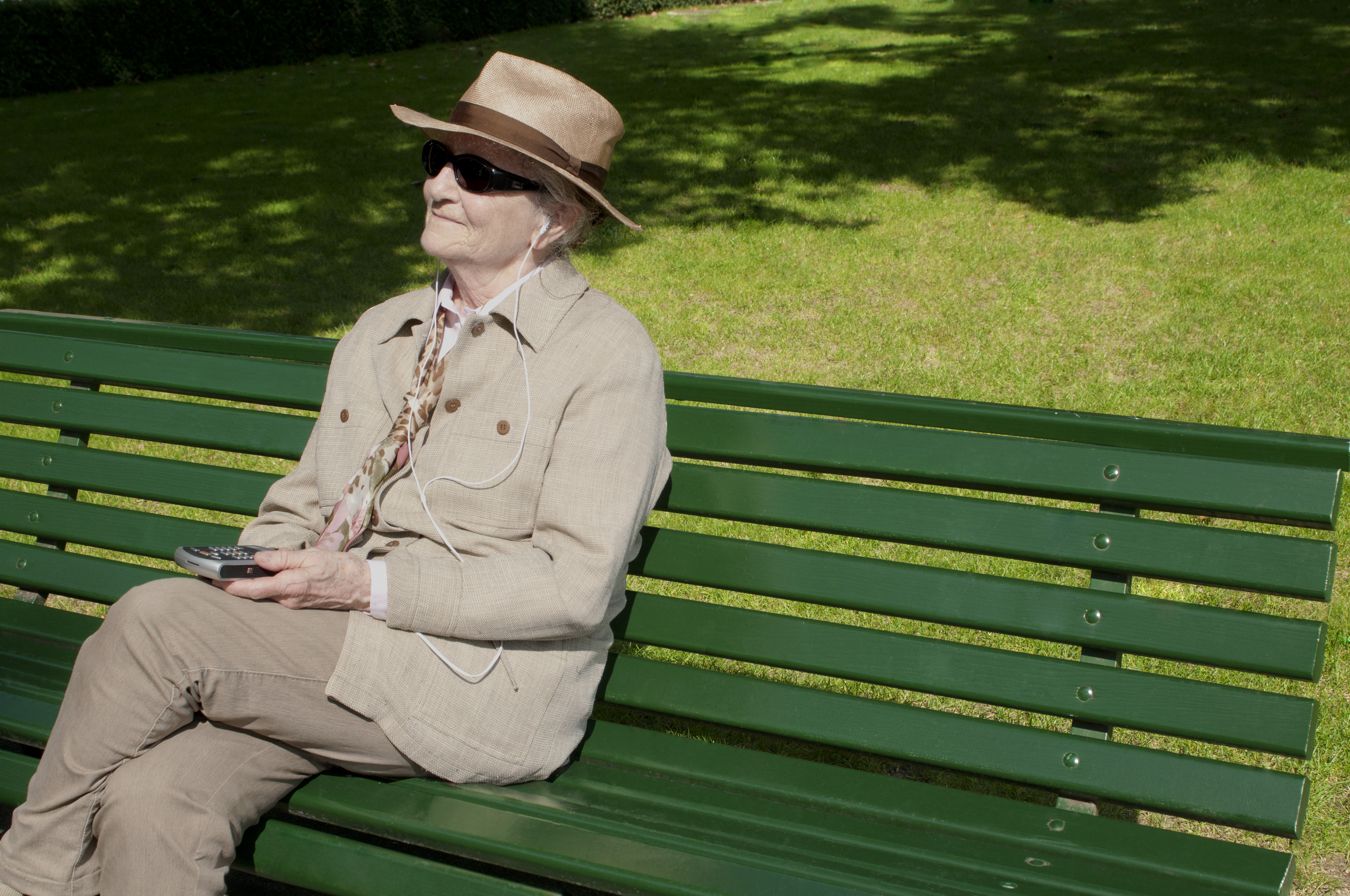 auditrice assise sur un banc dans un parc et écoutant un livre audio